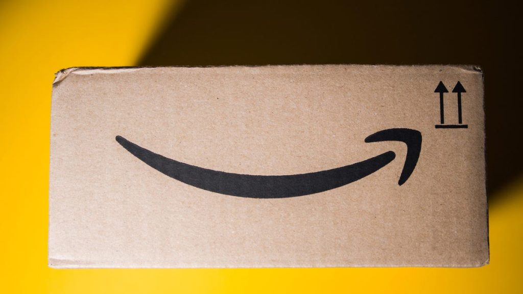 Amazon Got Busted for ‘Tricking’ You Into Prime. Now It’s Paying Out $2.5 Billion a side view of an old Amazon delivery box against a bright yellow background. the top left corner is covered in shade from the box's shadow