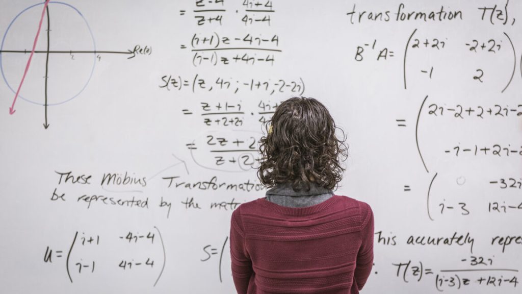 DeepMind’s latest: An AI for handling mathematical proofs A woman standing in front of a white board that is packed with equations.