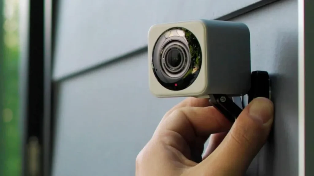 A hand adjusts a Wyze cam on exterior siding.
