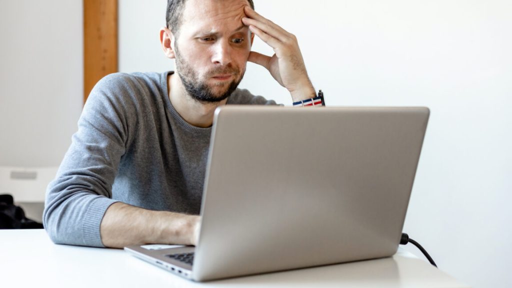 young man looking puzzled working at laptop