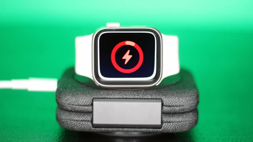 Apple Watch with white band charging on a dock, with a screen indicating low battery